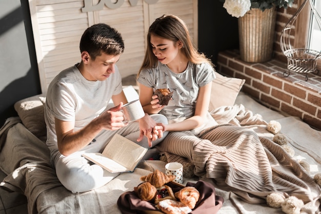 An overhead view of couple sitting on bed holding coffee cup and muffin in hand