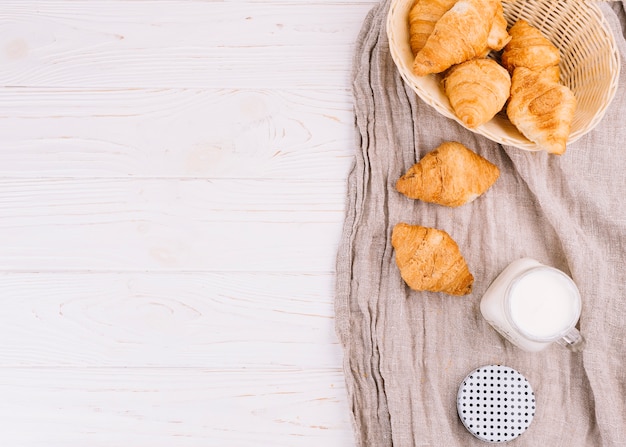 An overhead view of croissants and milk in mason jar on wooden backdrop