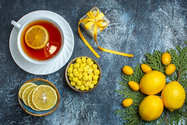 Free photo overhead view of a cup of black tea with lemon candies and gift box half whole citrus fruits collection on fir branches on dark background