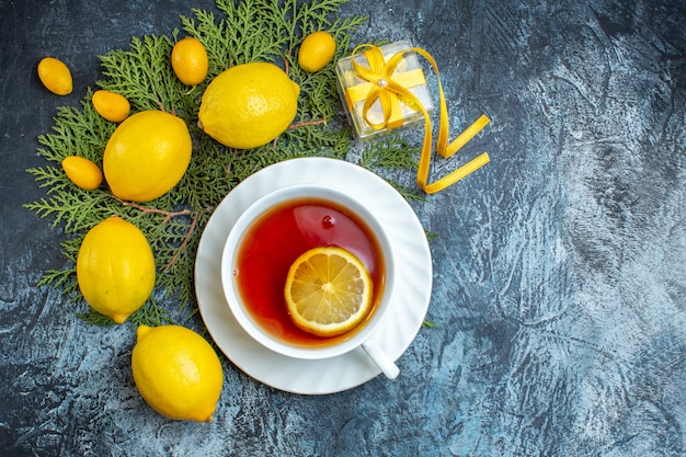 Free photo overhead view of a cup of black tea with lemon and collection of natural organic fresh citrus fruits on fir branches on dark background