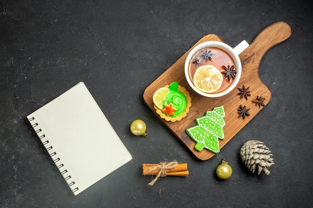 Overhead view of a cup of black tea xsmas accessories conifer cone and cinnamon limes notebook