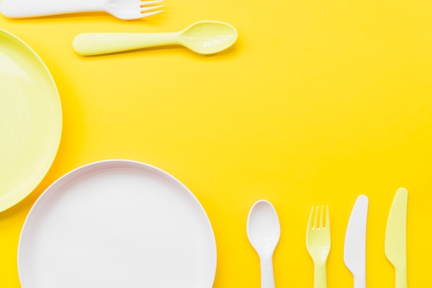 Overhead view of cutlery; plates on yellow background