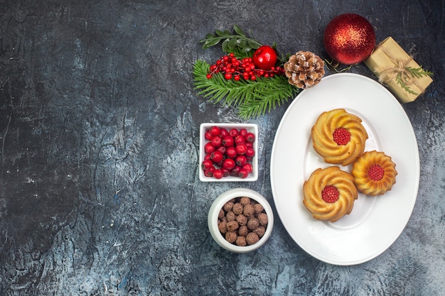 Overhead view of delicious biscuits on a white plate and new year decorations gift cornel in small pot chocolate on dark surface