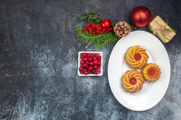 Overhead view of delicious biscuits on a white plate and new year decorations gift cornel in small pot on dark surface