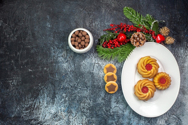 Overhead view of delicious biscuits on a white plate santa claus hat and chocolate in a bowl on dark surface