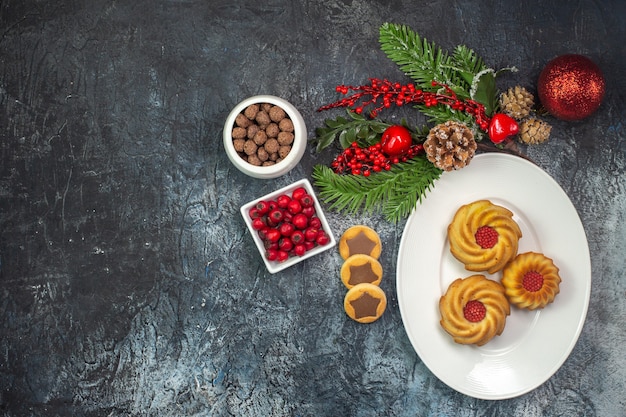 Overhead view of delicious biscuits on a white plate santa claus hat and chocolate cornel in a bowl decorations on dark surface