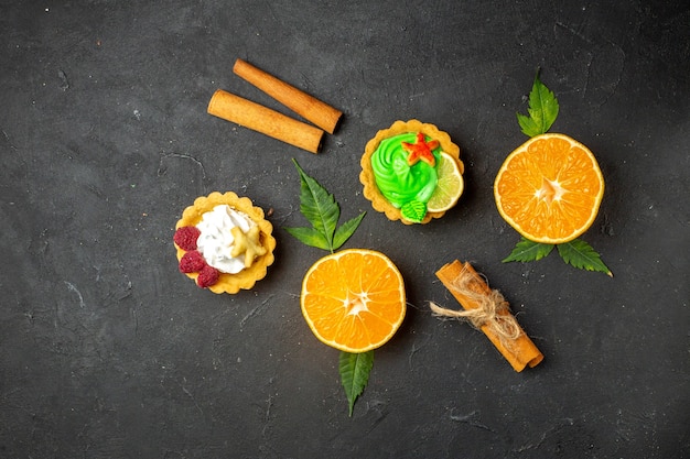 Free photo overhead view of delicious cookies cinnamon limes and half cut oranges with leaves on dark background