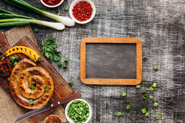 Overhead view of delicious grilled sausages and fresh ingredient with blank slate on wooden backdrop