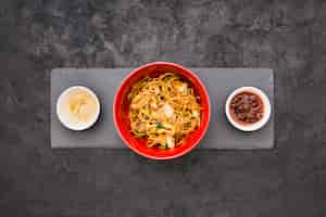 Free photo an overhead view of delicious noodles in bowl with sauce and marinated ginger over black slate stone