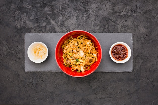 An overhead view of delicious noodles in bowl with sauce and marinated ginger over black slate stone