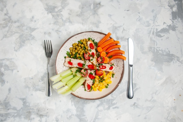 Overhead view of delicious salad with various ingredients on a plate and cutlery set on white surface with free space