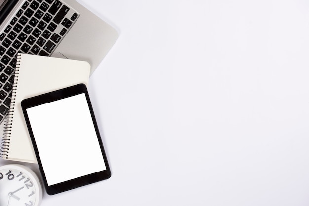 An overhead view of digital tablet; notepad on laptop with alarm clock isolated on white background