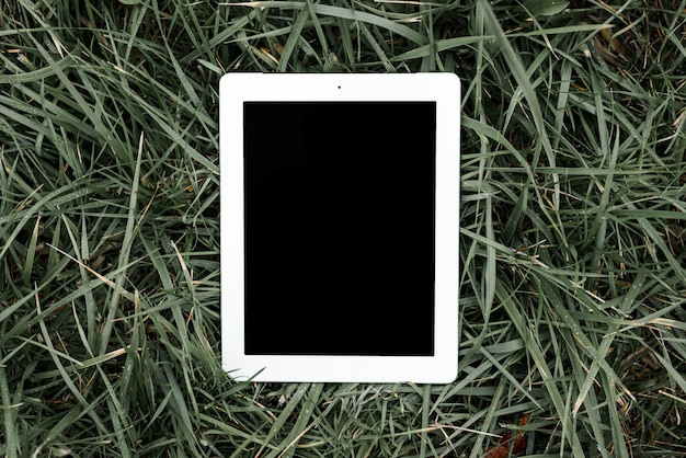 An overhead view of digital tablet with black screen on green grass