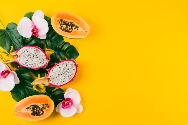 Free Photo an overhead view of dragon fruits; halved papaya with leaves and orchid flower on yellow backdrop