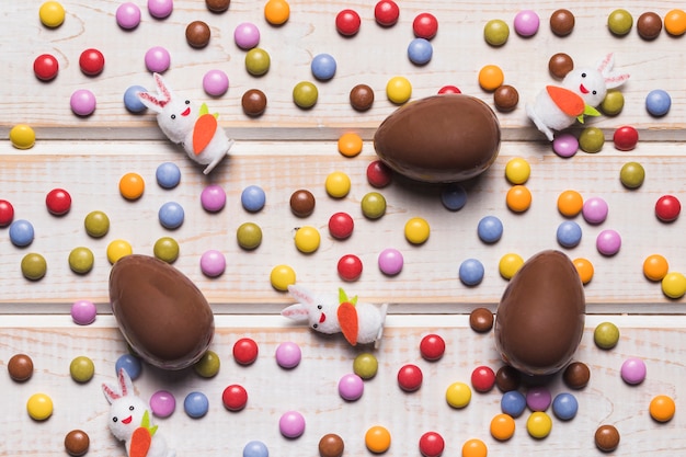 An overhead view of easter eggs and bunnies over the colorful gem candies on wooden desk