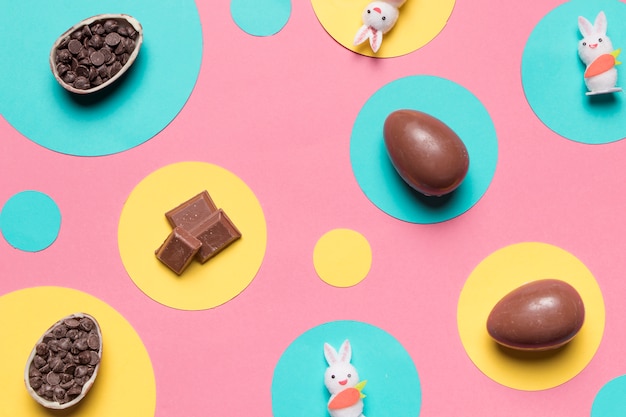 An overhead view of easter eggs; rabbit and choco chips on round frame over the pink background