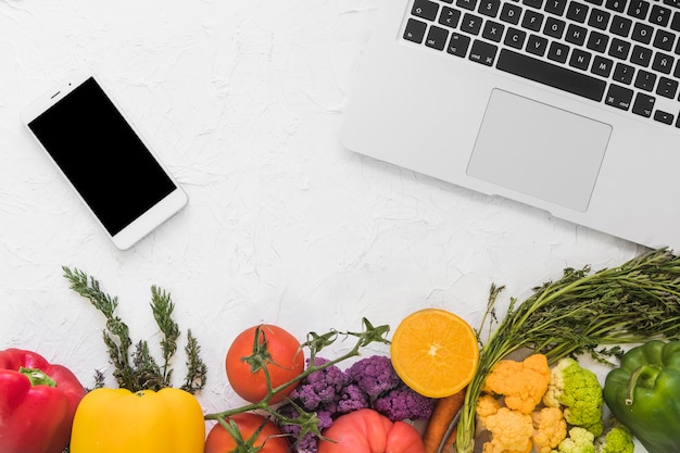 Free photo overhead view of electronic devices and vegetables on white surface