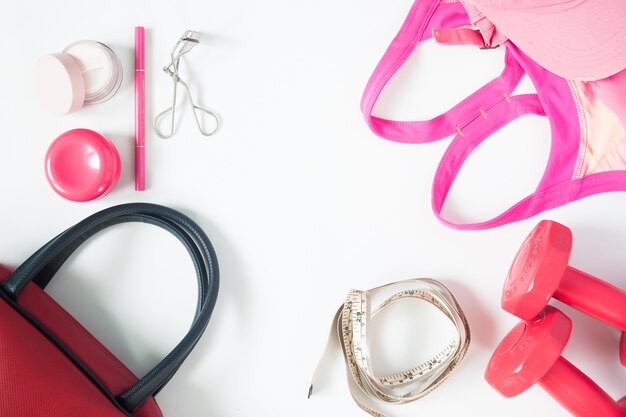 Overhead view of essential beauty items, Top view of red dumbbells, red hand bag and sport bra, flat lay isolated on white background