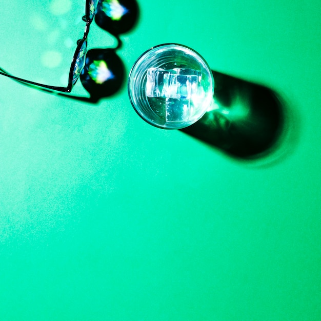 Free Photo an overhead view of eyeglasses and water glass with shadow on green background