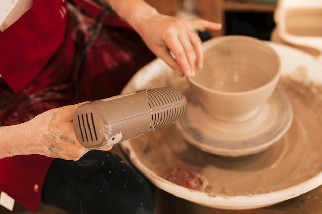 Free photo an overhead view of female potter drying the clay bowl with dryer