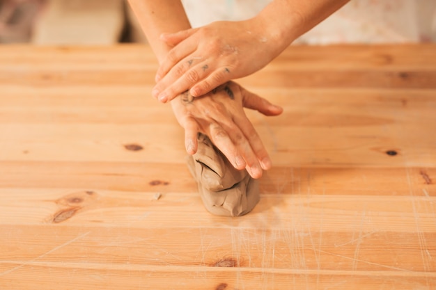 An overhead view of female's hands over the kneaded clay on wooden table