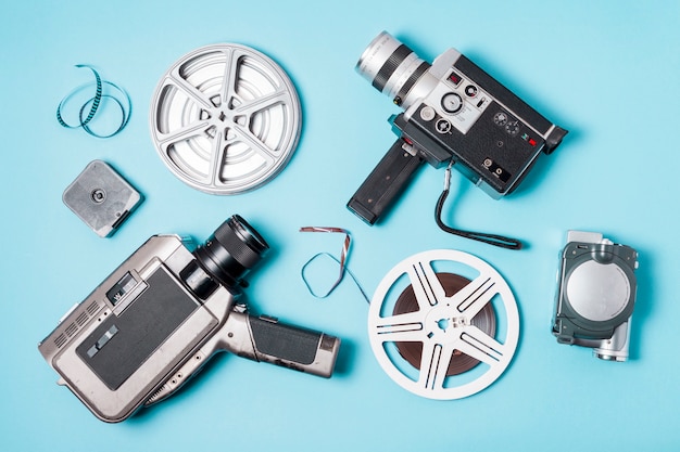 Free photo an overhead view of film strips; film reel and various type of camcorder on blue background