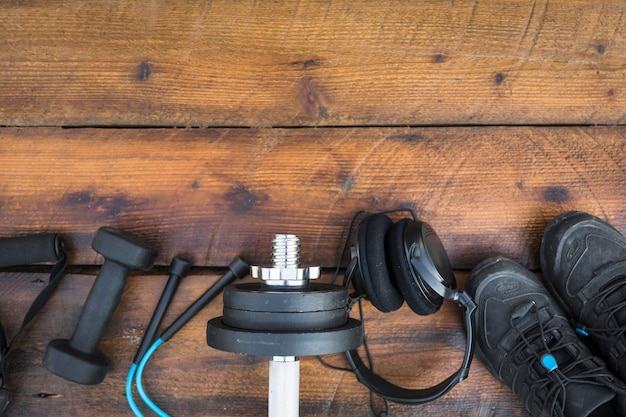 Free Photo an overhead view of fitness strap; dumbbells; skipping rope; weights; headphone and shoes on wooden textured background