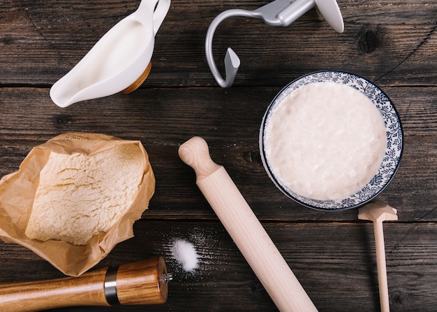 Free photo an overhead view of flour; milk; yeast and peppermill with rolling pin on table