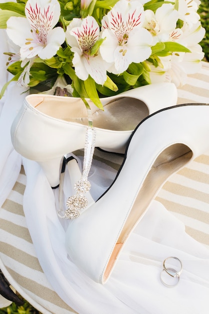 An overhead view of flowers; high heels; crown; scarf and wedding rings on table