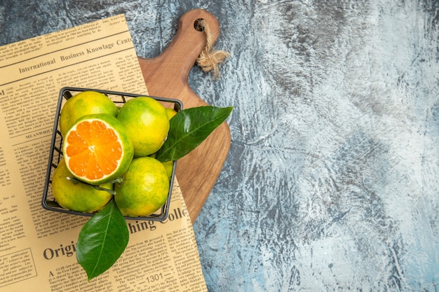 Free Photo overhead view of fresh citrus fruits newspaper on wooden cutting board on gray background