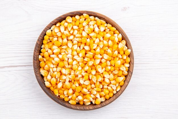 Overhead view of fresh corn kernels in a brown bowl on white background