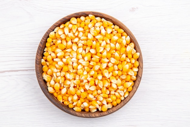 Overhead view of fresh corn kernels in a brown bowl on white background