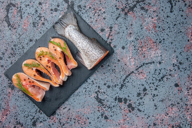 Overhead view of fresh cut raw fishes green on dark color tray on the left side on blue black mix colors table with free space