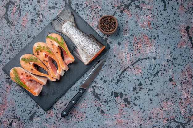 Overhead view of fresh cut raw fishes green on dark color tray pepper knife on blue black mix colors table with free space