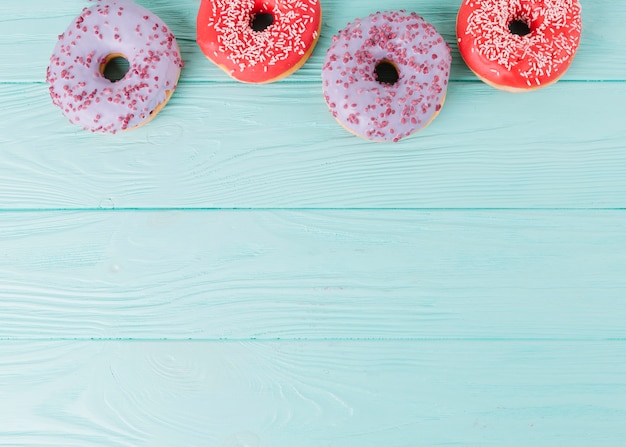 An overhead view fresh donuts arranged in a row on wooden table