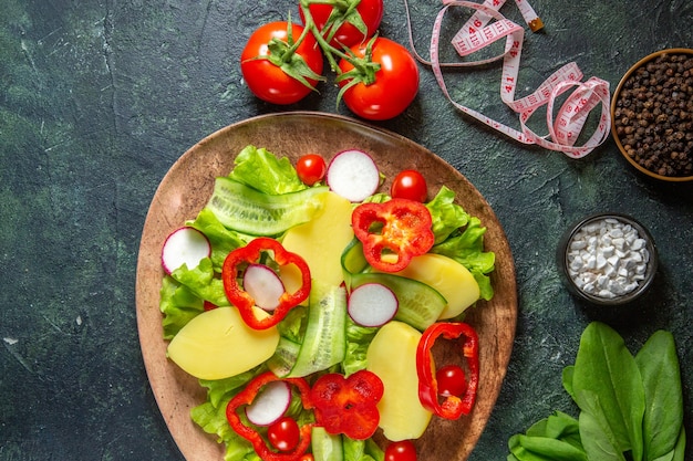 Free photo overhead view of fresh peeled cut potatoes with red pepper radishes green tomatoes in a brown plate and meters spices on green black mix colors surface