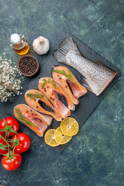 Free photo overhead view of fresh raw fishes greens pepper and lemon slices on dark color tray oil bottle vegetables on mix colors table