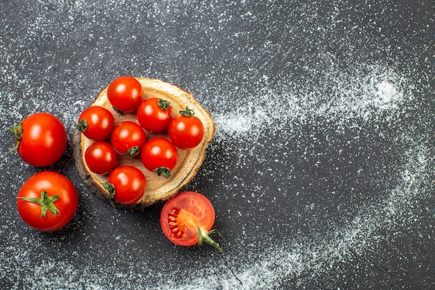 Overhead view of fresh tomatoes with stems on wooden board on the right side on white black background