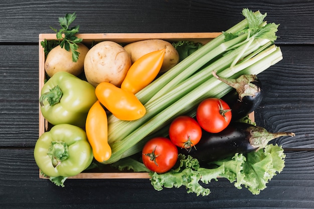 Free photo overhead view of fresh vegetables in container on black wooden background