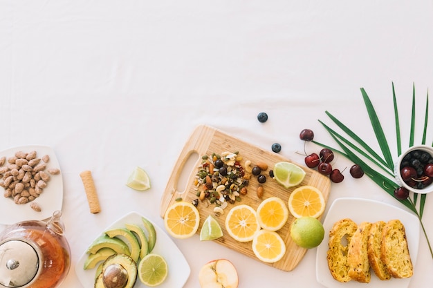 An overhead view of fruit; tea; bread and dry fruits on white background