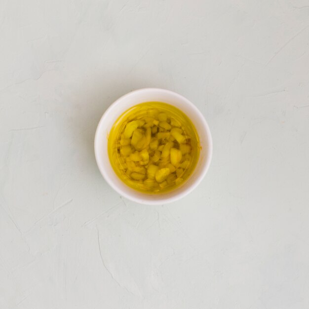 An overhead view of garlic infused olive oil in bowl on white textured background