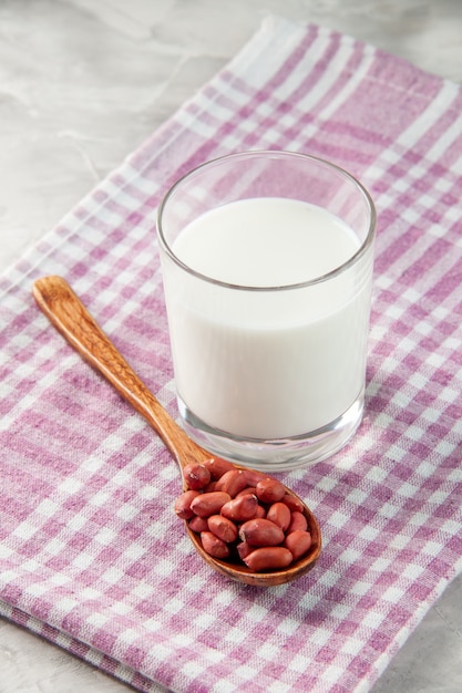 Overhead view of glass cup filled with milk and peanuts in spoon on purple stripped towel