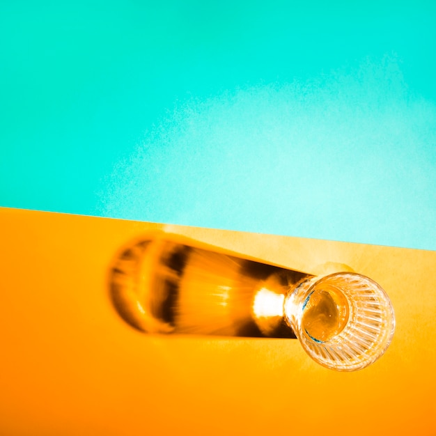 Free photo an overhead view of glass with bright shadow on yellow and turquoise background