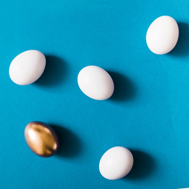 Free photo overhead view of golden egg among the white eggs on blue background