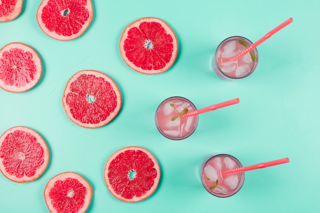 An overhead view of grapefruits slices and glass of juice with ice and mint on pastel background