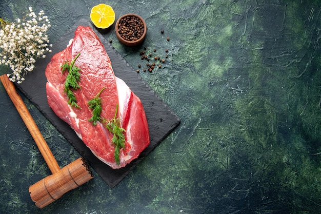 Overhead view of green on fresh red raw meat cutlery set on cutting board and pepper lemon wooden hammer on green black mix color background