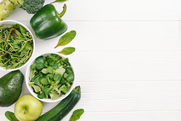 Free photo an overhead view of green healthy fresh vegetables on white wooden desk