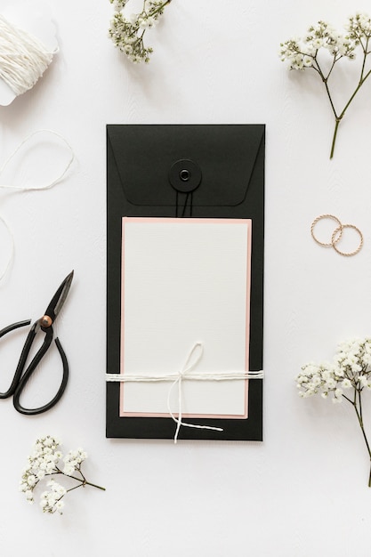 Free photo an overhead view of greeting cards with scissor; wedding rings; string and flower on white background