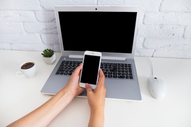 Overhead view of hand holding smartphone over the laptop