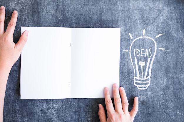 Overhead view of hand holding white card near the drawn idea bulb on chalkboard